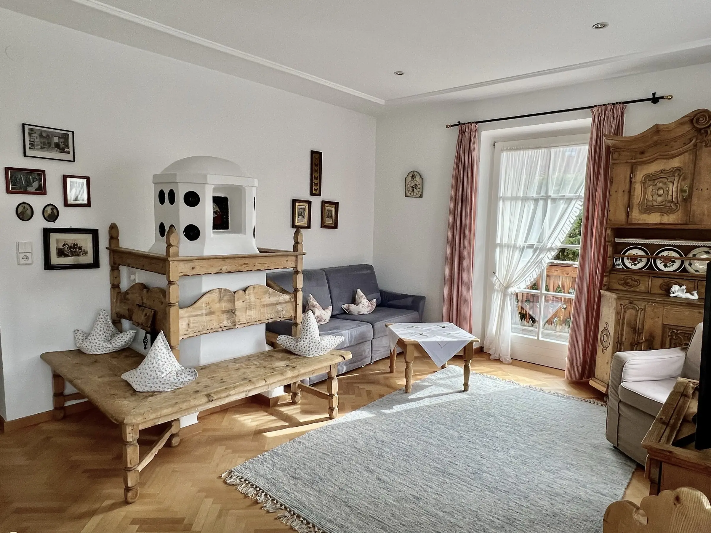 Apartment 4 – Wohnzimmer mit Kachelofen, Sofa und Balkontür